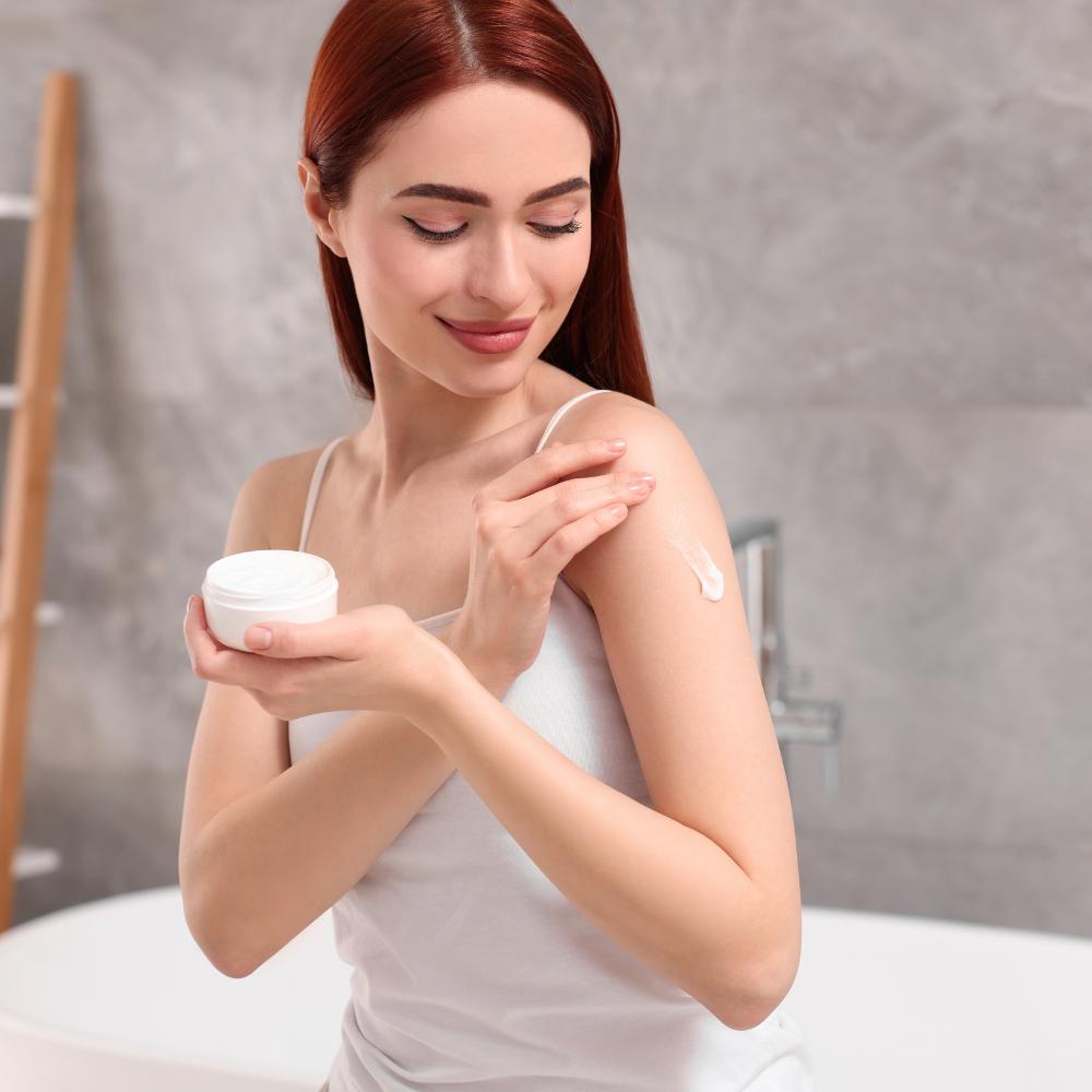 Woman applying cream to her arm in a bathroom setting

