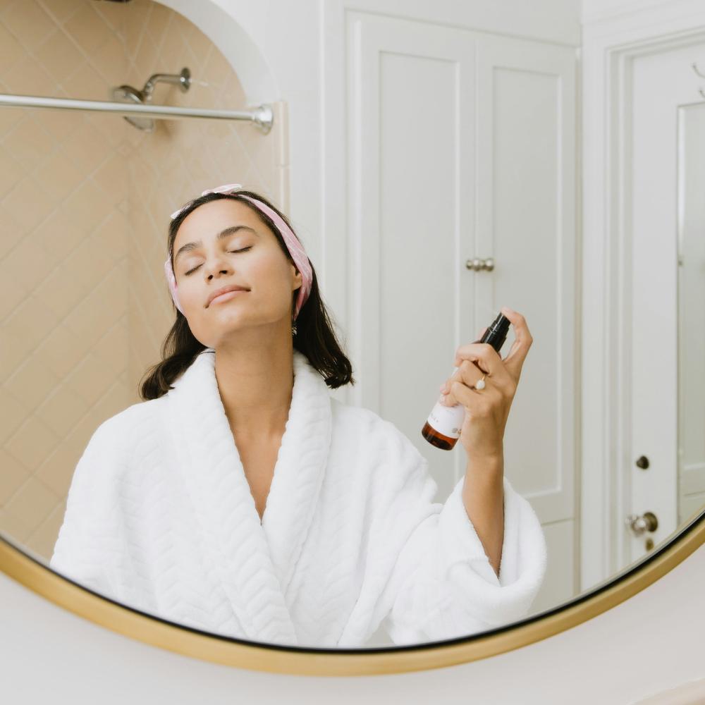 Woman in a white robe applying sunscreen in front of a mirror

