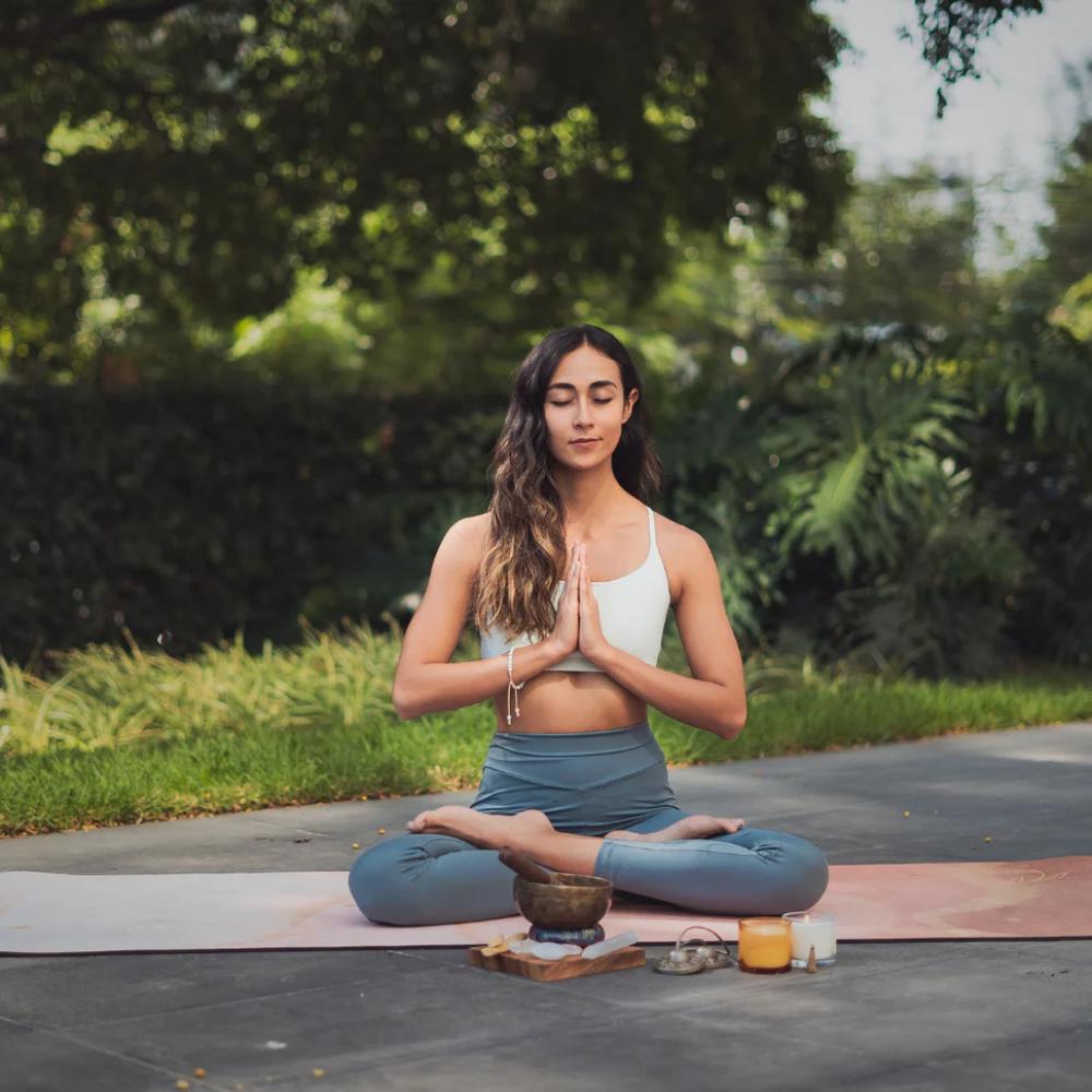 Woman meditating outdoors with greenery in the background

